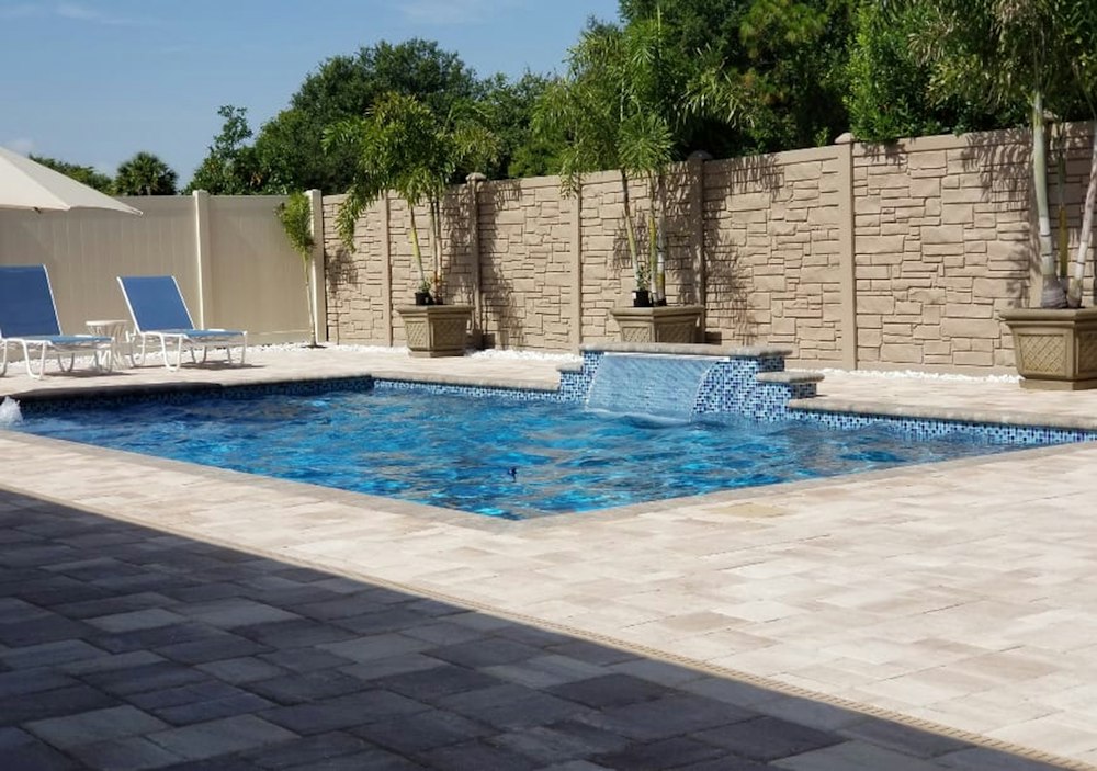 Piscina con reposeras junto a un muro de piedra, contacto de Piscinas y Terrazas