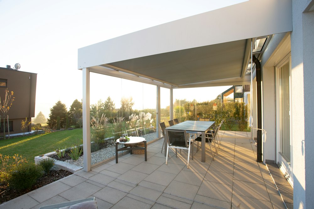 Terraza techada con estructura blanca y mesa de comedor